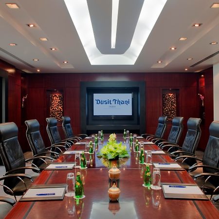 Dusit Thani Dubai Exterior photo The photo shows a sleek and modern conference room. It features a long wooden table surrounded by black leather executive chairs. At the center of the table, there is a decorative arrangement of green plants. On the table, there appear to be glass bo