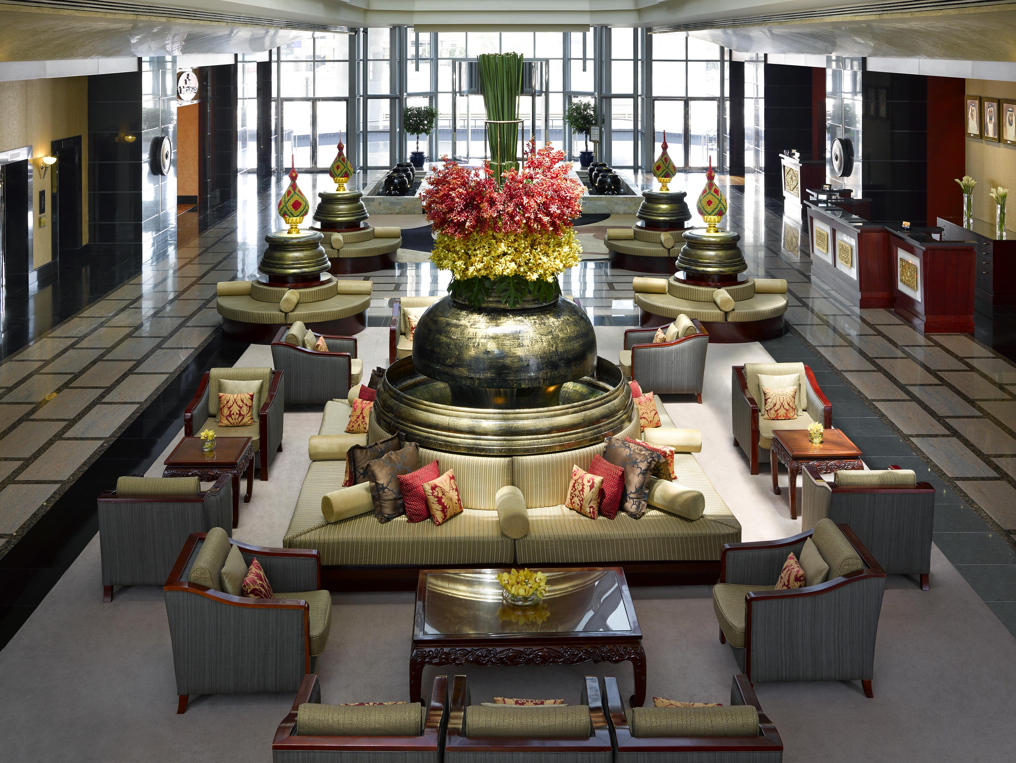 Dusit Thani Dubai Exterior photo The photo shows a spacious hotel lobby that features elegant design elements. Central to the space are large decorative arrangements, including tall vases filled with vibrant flowers. The area is adorned with multiple seating arrangements composed of