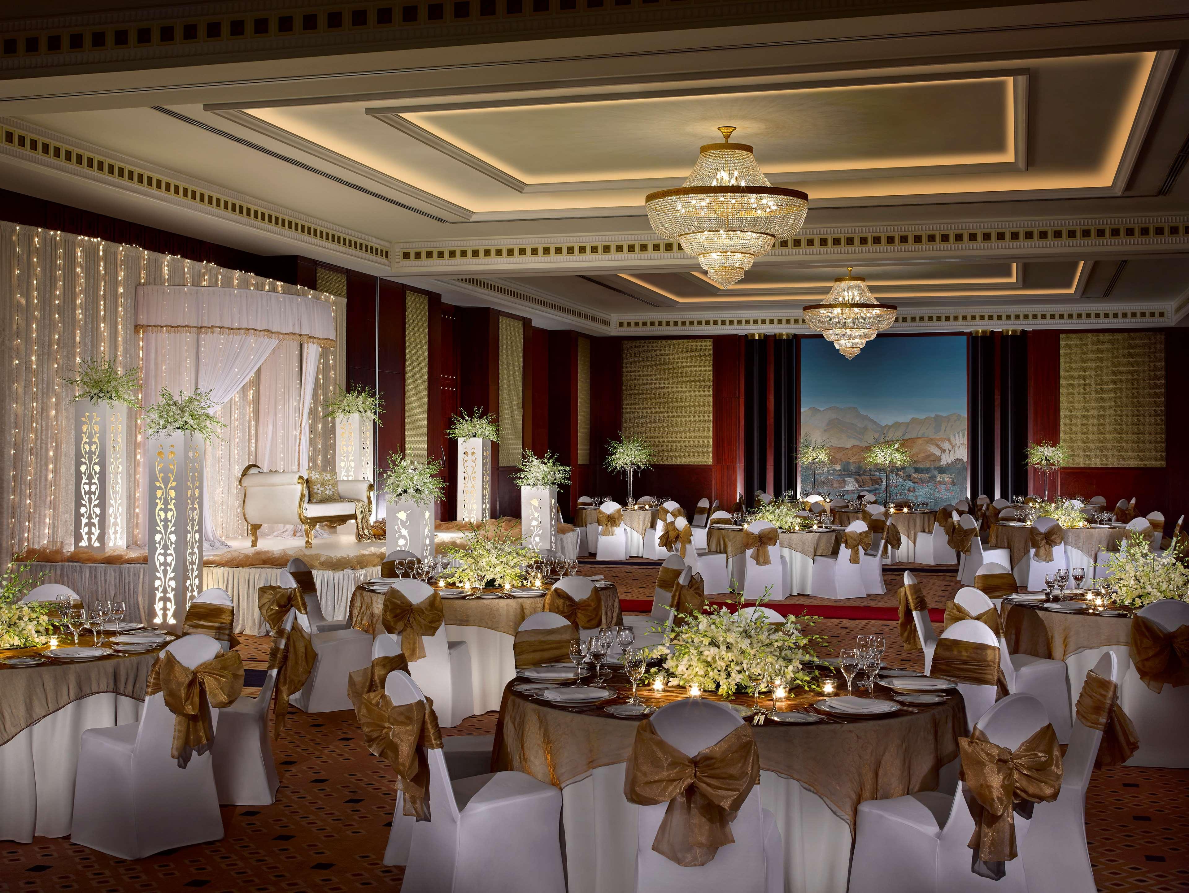 Dusit Thani Dubai Exterior photo The photo shows a beautifully decorated banquet hall, likely set up for a wedding or formal event. The room features elegantly arranged tables covered with white tablecloths and adorned with floral centerpieces. Each chair is draped in a white cover 