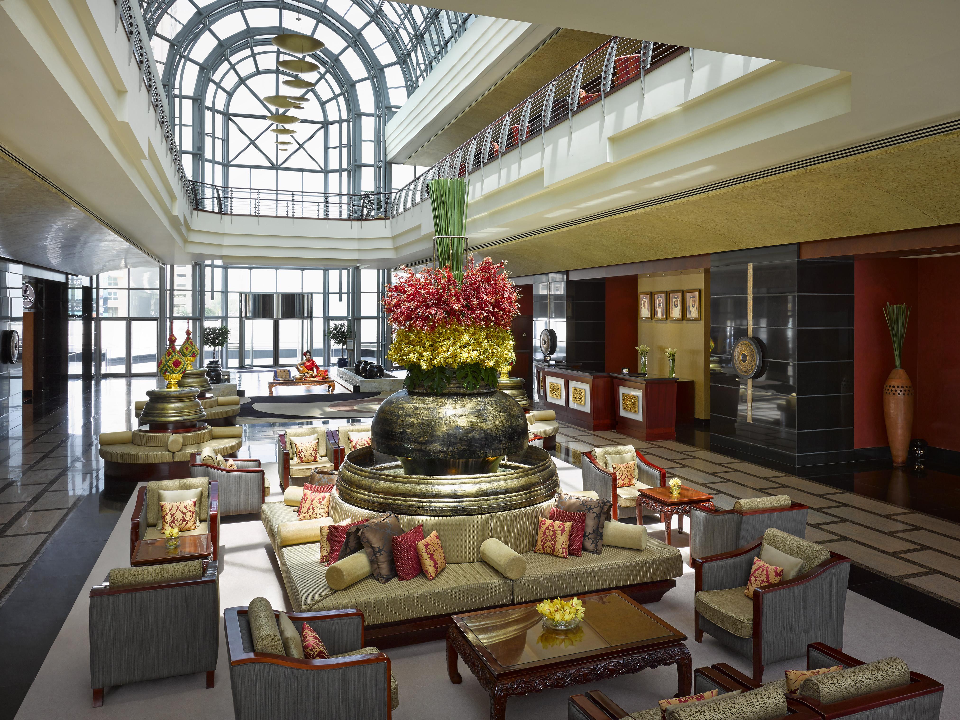Dusit Thani Dubai Exterior photo The image shows a luxurious hotel lobby characterized by a spacious, elegant design. It features high ceilings and large windows that allow natural light to flood the area. There is an impressive water feature, which includes a large, circular base a