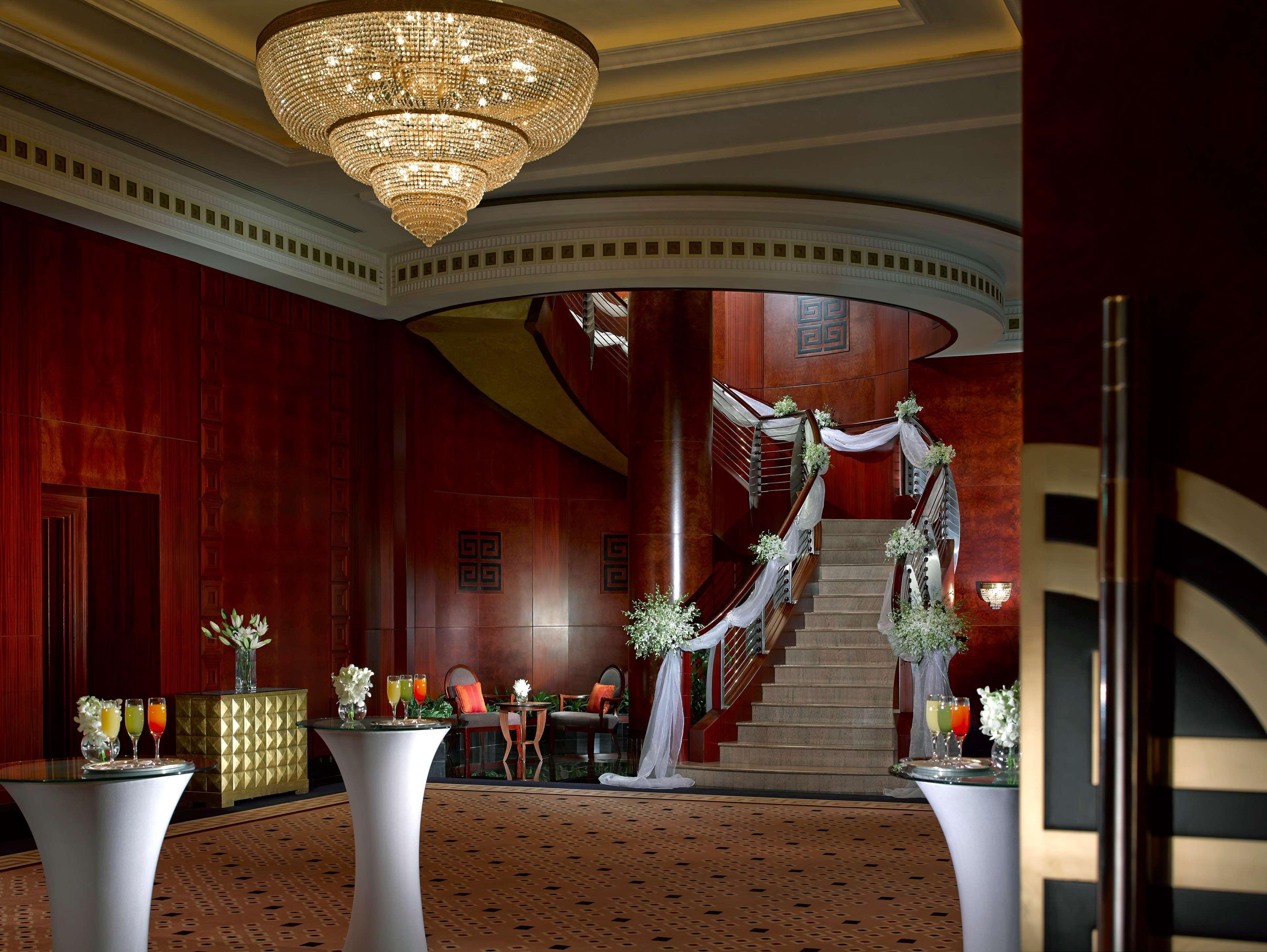 Dusit Thani Dubai Exterior photo The photo depicts an elegant interior space, likely a hotel or event venue. It features a grand staircase with a beautifully designed railing, leading to an upper level. The walls are rich in wood paneling, creating a warm atmosphere. Luxurious chand