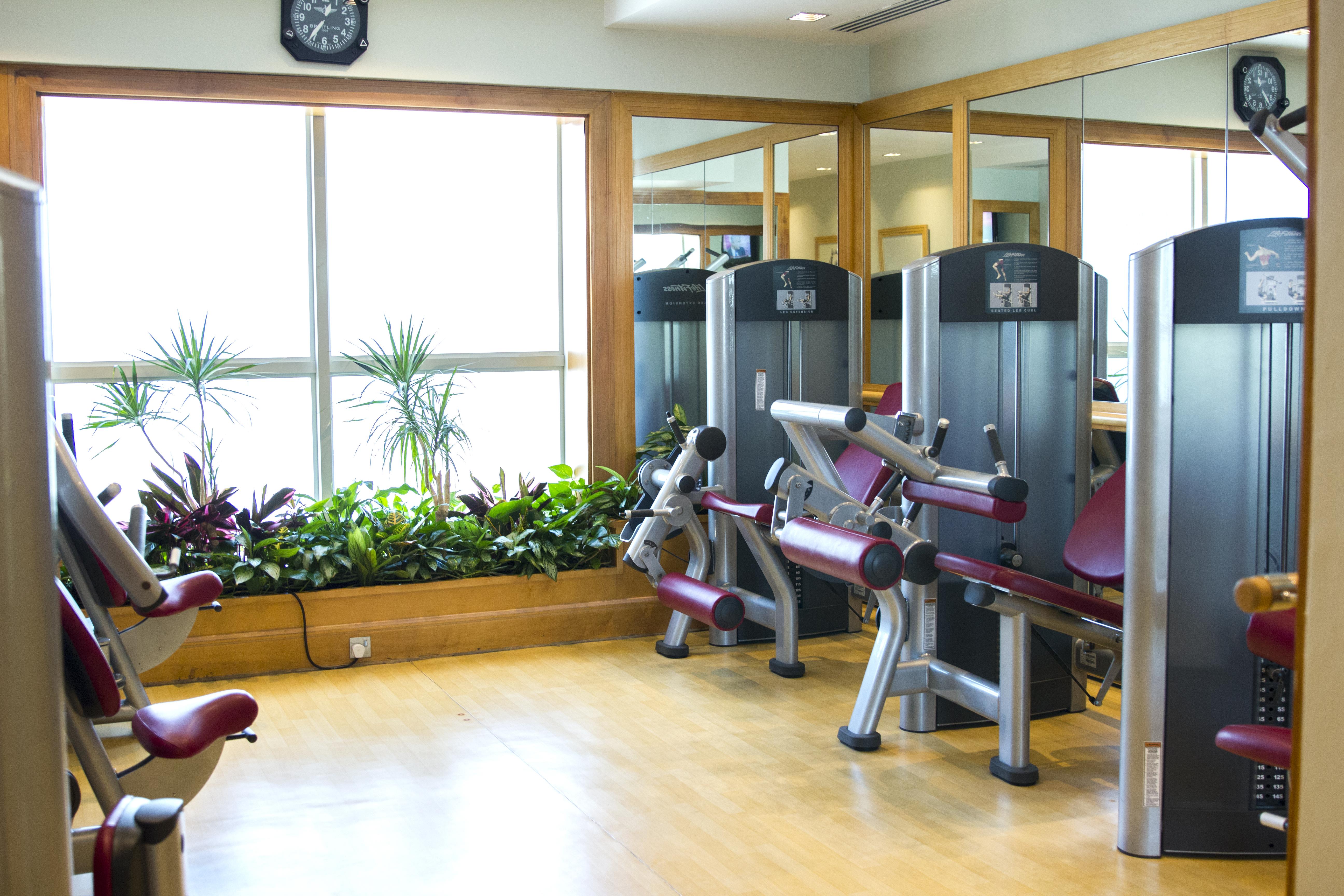 Dusit Thani Dubai Exterior photo The photo shows a modern fitness gym with several exercise machines. The room has large windows that let in natural light, along with some greenery visible outside. There are plants along the base of the windows, adding to the welcoming atmosphere. T