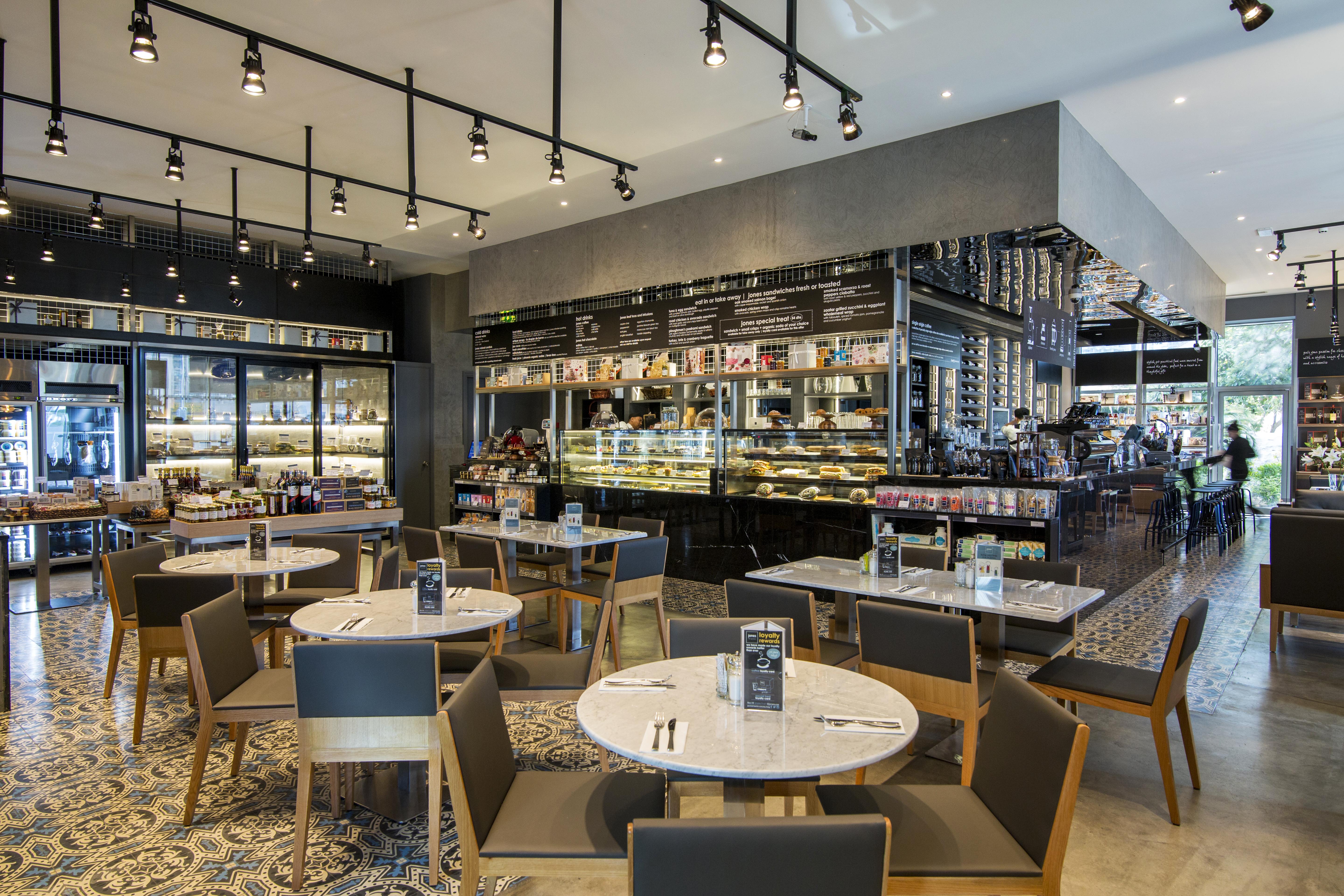 Dusit Thani Dubai Exterior photo The photo shows a modern restaurant or café interior. It features several round tables with white marble tops and wooden bases, surrounded by gray upholstered chairs. The space is well-lit with hanging lights and has a stylish, contemporary design.

