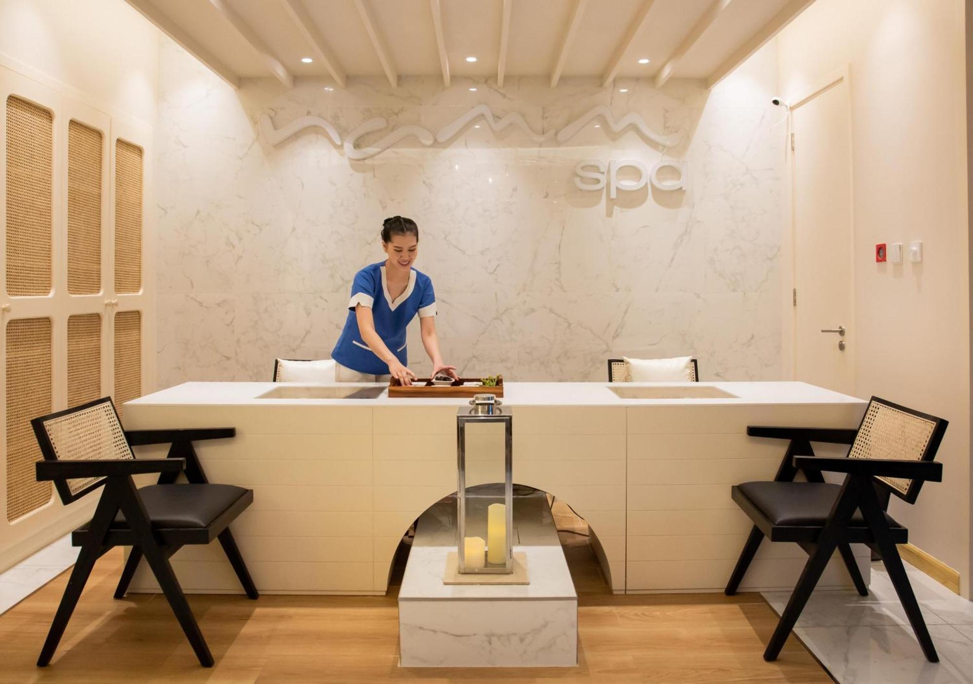 Dusit Thani Dubai Exterior photo The photo depicts a serene spa reception area. In the center, a staff member is seen preparing for services at a modern reception desk adorned with a marble surface. The background features a sleek, light-colored design with the word "spa" elegantly 